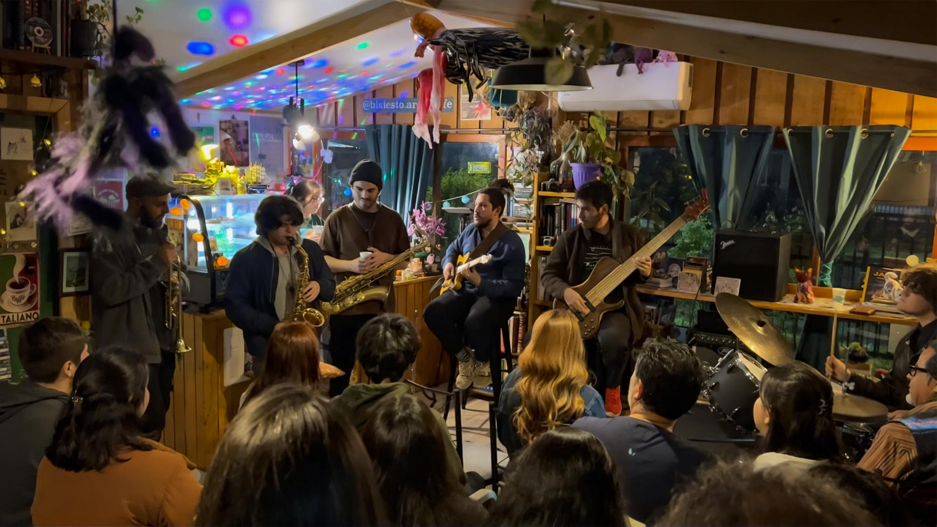 Un grupo de unas 25 personas escucha una jam session entre el grupo de jazz invitado "Equinopsis" y un grupo de jóvenes músicos locales.