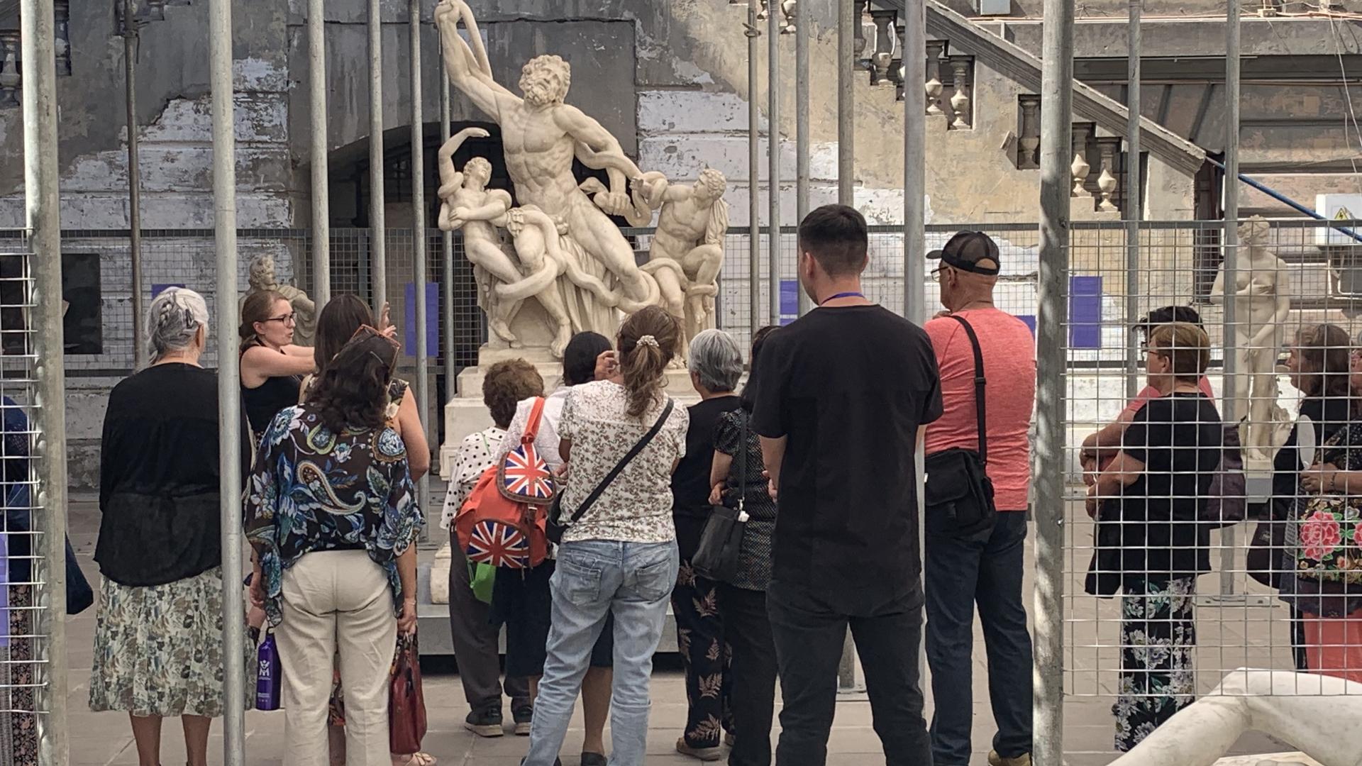 Grupo de personas que participa de un recorrido mediado en Patio Paulonia, se encuentran junto a la escultura Laocoonte y sus hijos, copia en mármol de esta obra clásica.